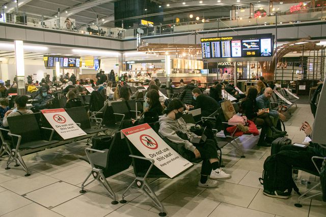 Many travelers sit in a departure lounge, while socially distanced